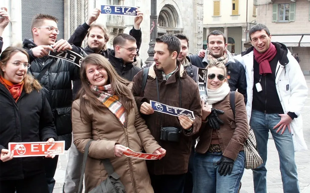 A group of young people in a town square, laughing and holding up ETZ stickers